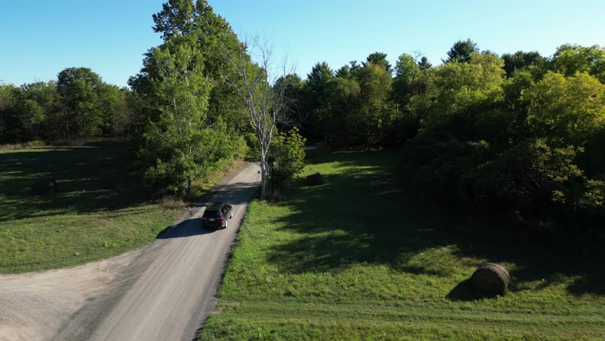Aerial approach over rural road cutting through forested Sacacomie countryside, tracking follows SUV driving on dirt path into trees