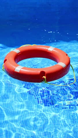 Bright orange life preserver floats in pool water, sun's rays creating shimmering waves. Lifesaving equipment ensures safety. Drowning prevention. Water rescue equipment