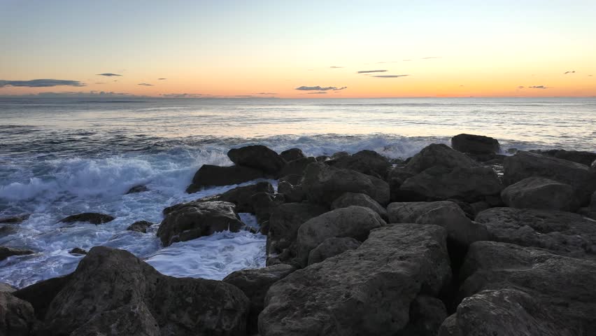 Dark coastal rocks surrounded by Atlantic waves under soft sunset sky, textured sea surface and natural contrast
