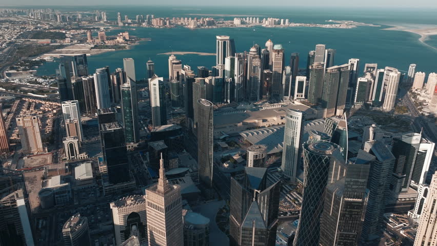 Aerial view of Doha Qatar at golden hour with the sun setting over the skyline and skyscrapers casting long shadows across the city and the Arabian Gulf