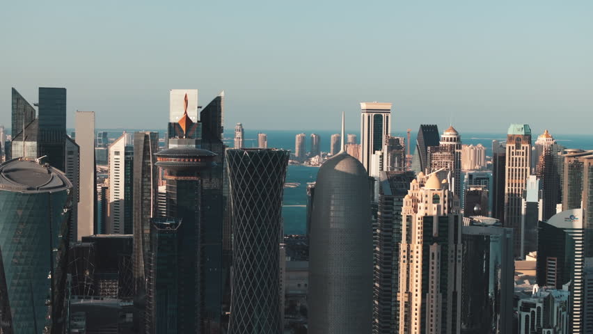 Aerial view of Doha Qatar at golden hour with the sun setting over the skyline and skyscrapers casting long shadows across the city and the Arabian Gulf