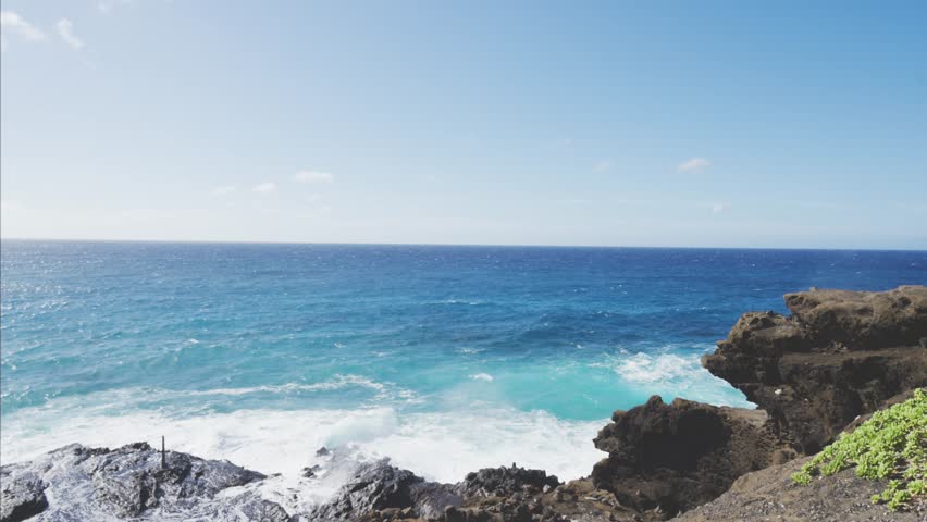 Turquoise ocean water with beautiful white waves crashing against a dramatic volcanic rock cliff coast on a sunny day in honolulu, hawaii, creating a powerful and scenic natural seascape