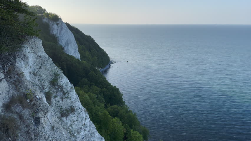Stralsund, Mecklenburg-Vorpommern, Germany - August 20, 2025: Static aerial view of the iconic white chalk cliff formations of Jasmund National Park overlooking the Baltic Sea with dense forest coverage on the cliff edge.