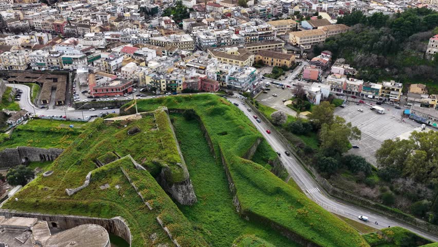 Aerial view of the New Fortress of Corfu with green ramparts and city traffic during a cloudy day, historic Venetian fortification in Greece
