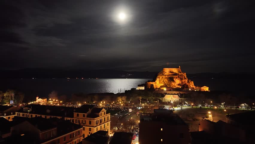 Night view of the illuminated Old Fortress of Corfu, Greece. Venetian castle Palaio Frourio at nighttime with city lights, sea reflection, and historic architecture in Kerkyra old town at dusk. 4K