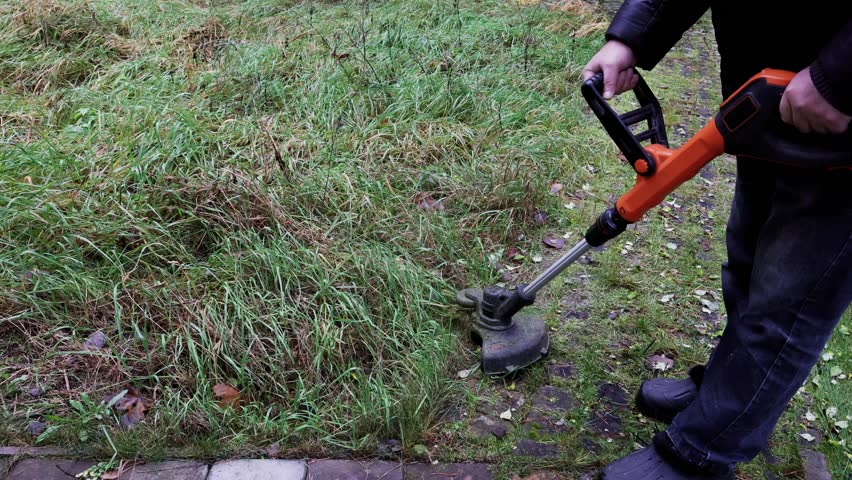 Man cuts grass with cordless hand-held lawn trimmer with line, top view. High quality 4k footage