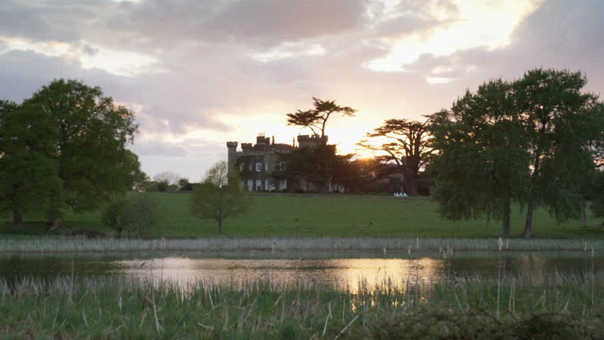 Picturesque view of a historic castle on a grassy hill during a beautiful sunset over a lake