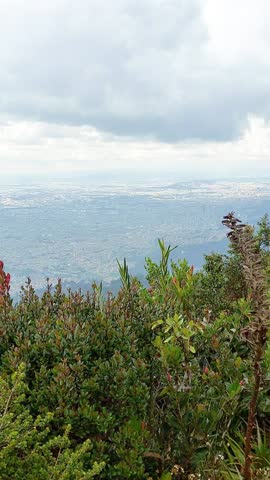 Panoramic view of a dark mountain silhouette and city lights under a vibrant orange and blue twilight sky at dusk.