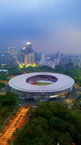Jakarta, Indonesia – November 10, 2025: Aerial view of Gelora Bung Karno Stadium surrounded by green park and modern skyscrapers during evening time, showcasing Jakarta city skyline and urban atmosphere in Indonesia’s capital.
