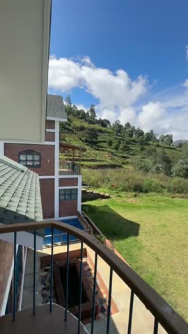 Beautiful green hillside landscape with blue sky and clouds, viewed from a balcony in a peaceful countryside location.
