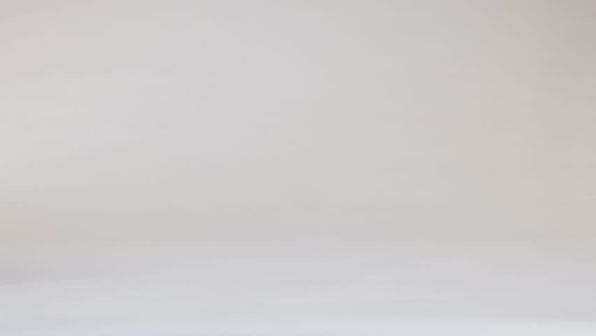 A white baseball bounces and rolls across a clean white studio floor under soft lighting