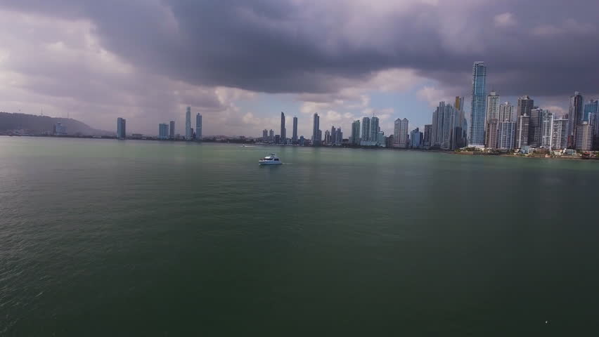 Drone shot showing a boat moving away from the Panama City skyline across the bay under dark storm clouds.