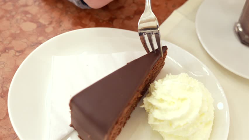 Chocolate cake slice with whipped cream and fork on white plate