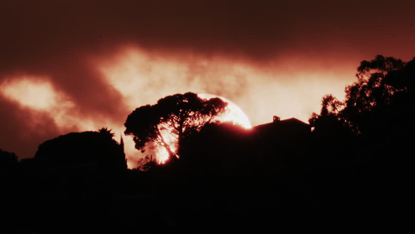 A glowing red sun partially covered by dark clouds at dusk