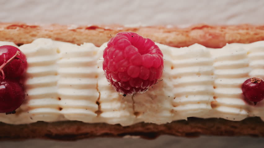 Close up of a gourmet pastry topped with cream, raspberries, and red currants