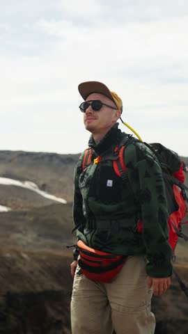 Solo hiker with camera trekking across rugged volcanic landscape, wearing backpack and outdoor gear, exploring remote highlands under cloudy daytime sky