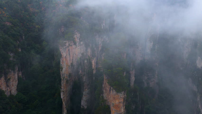 Low Clouds And Mist Blanketed Towering Pillars Of The Zhangjiajie National Forest Park In China. Aerial Shot