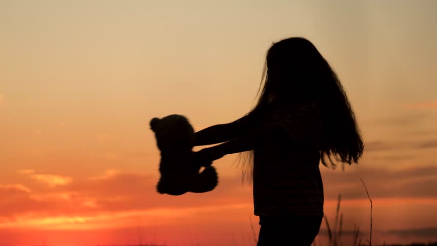 Young daughter silhouette with teddy bear, child playing at sunset, soft plush toy, dreamy orange sky, nature field background, small girl, outdoor childhood, fantasy and dreams, tender playtime, calm