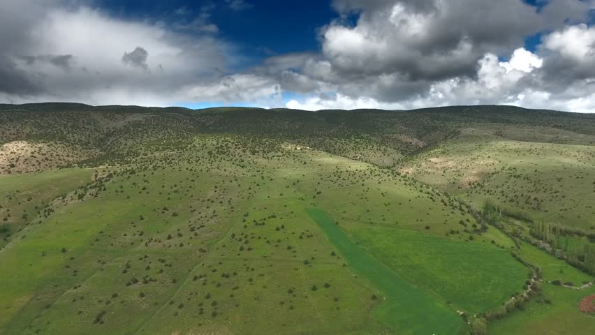 Aerial view of North African hills with green meadows and sparse shrubs under clouds. Elevated panorama shows rolling highlands, lush grassland patches, scattered bushland, storm sky.