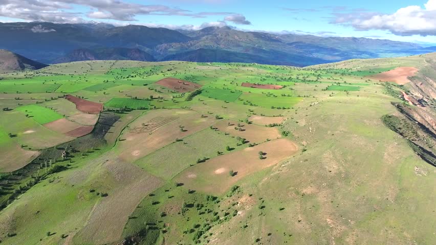 Cinematic aerial view shows sparse trees across green plateau fields on Anatolian highlands Turkey. Wide farmland patterns stretch over mesa butte ridge terrain beneath dramatic clouded skies