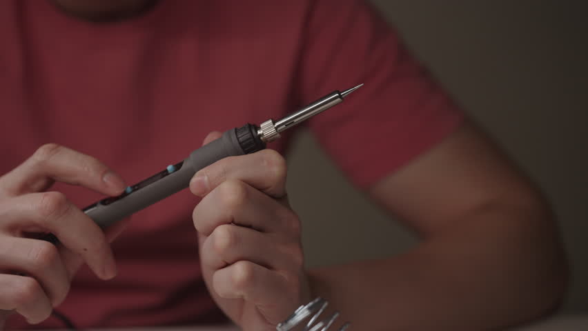 Electrician holding electric soldering iron, adjusting settings, preparing for intricate electronic repairs, hobbyist engaging in diy circuit building and maintenance, close-up, slow motion.