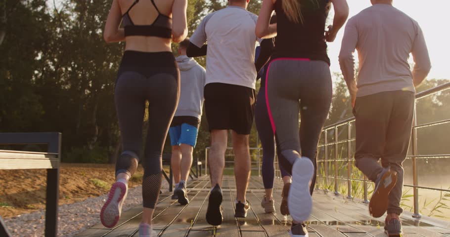 Back view of a team of young people running together in summer park having sport workout outdoors. Group of runners training in nature jogging in park. Healthy lifestyle and fitness concept. 4k video