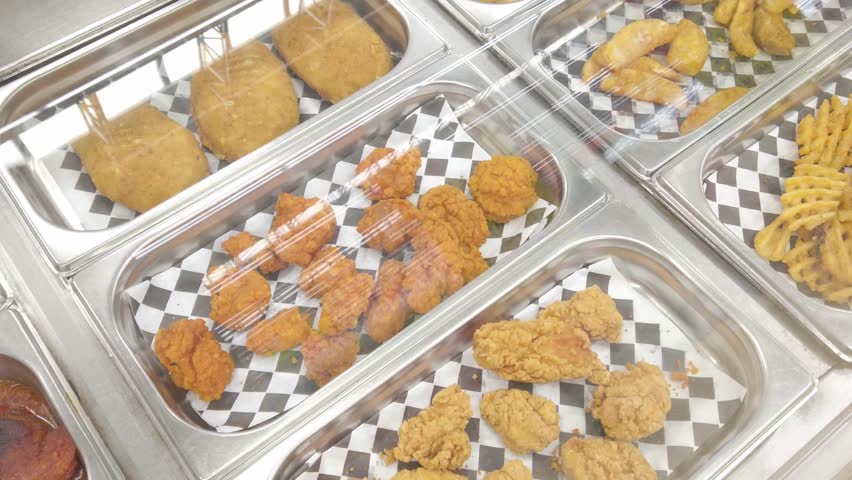 Pan left shot across fried food trays at cafeteria counter.