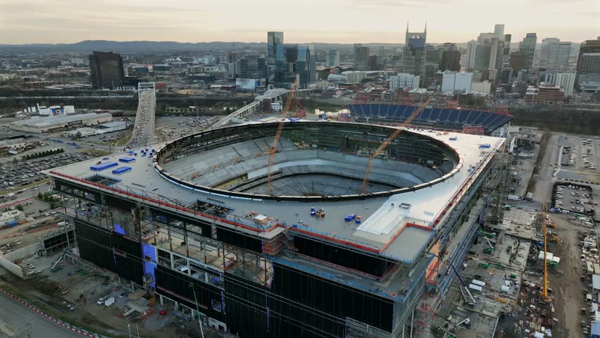 Downtown Nashville at sunset, with city skyline and new large stadium under construction, with cranes, urban development and golden evening light. Drone wide shot.
