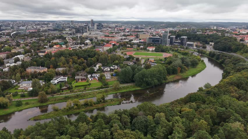 Aerial view pulling back from riverbank with trees and Vilnius city behind