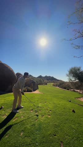 Golfer hits long iron on par 3 at dusk on Arizona desert golf course, vertical sunny day 4k