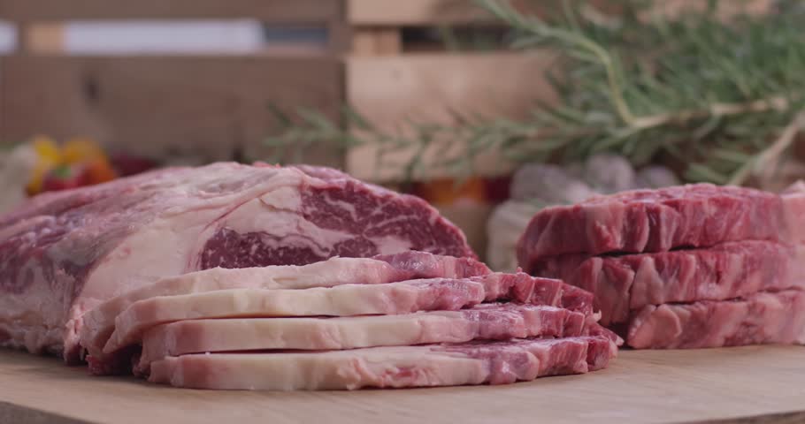 Close up of fresh raw marbled beef ribeye slices and steak medallions on a wooden cutting board with rosemary.