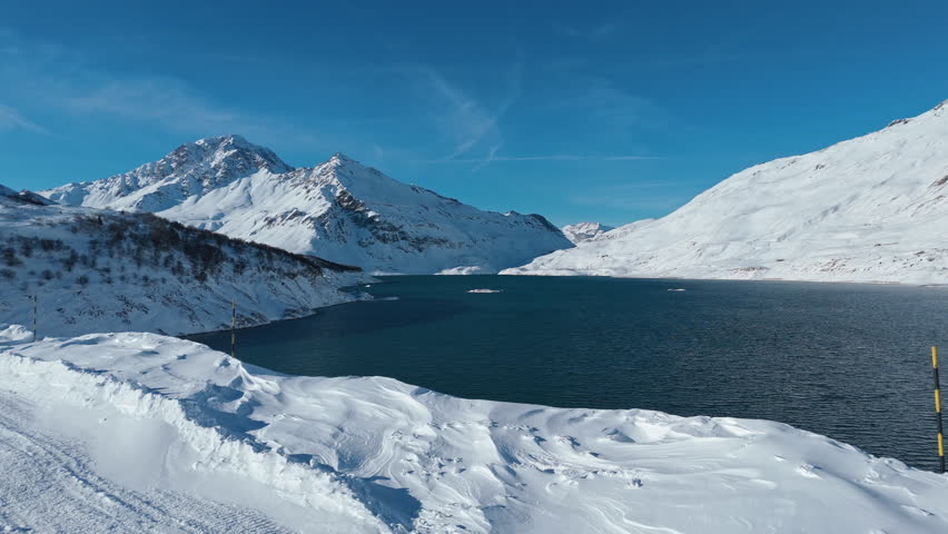 Snowy mountains by a lake with people skiing under a clear blue sky