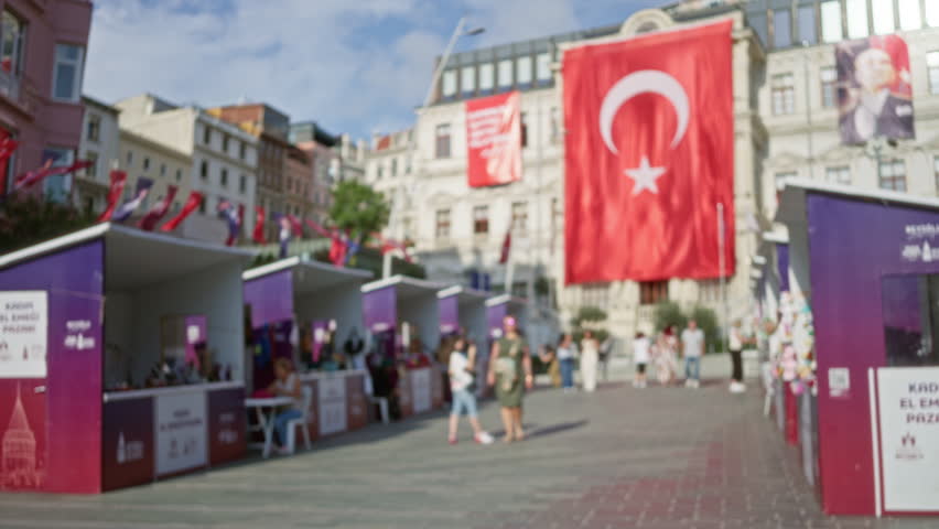 Blurred street market scene in istanbul with defocused vendor stalls, large hanging flag and tiled pavement, shallow bokeh street background; background copyspace backplate template.