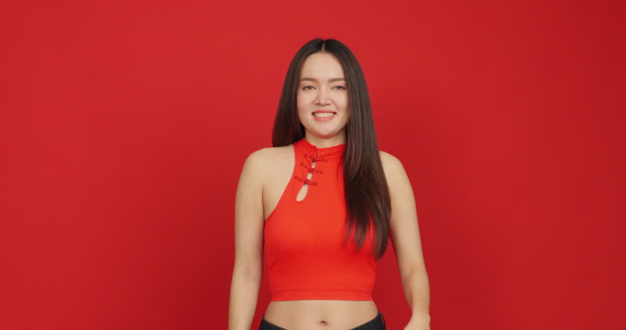 Happy young Asian woman in red Chinese dress gesturing to copy space on red background for Chinese New Year.