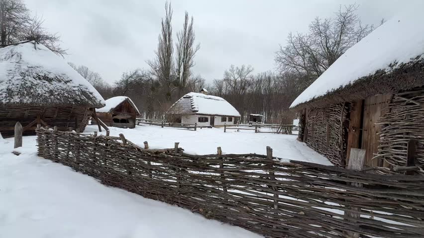 An ancient Ukrainian hut with a thatched roof and authentic courtyard decorations in a winter landscape of the 18th–19th centuries.