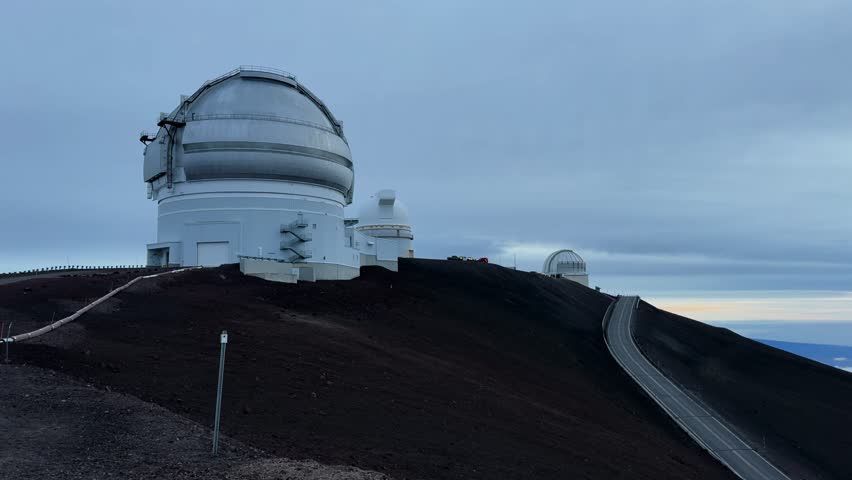 Panning view of Mauna Kea observatory domes and access road at dusk.