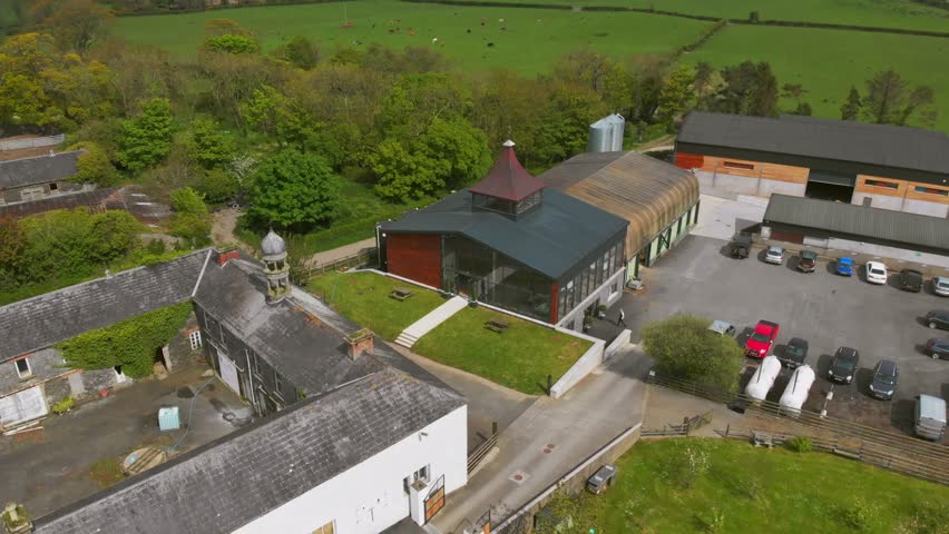 Aerial view of an industrial distillery complex with modern buildings, glass frontage, service yard, and surrounding farmland, shot in Belfast, Northern Ireland.