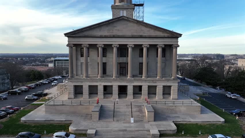 Tennessee State Capitol in Nashville, showing historic neoclassical architecture rising above city with skyline in background at daylight. Aerial rising shot. Flag of America and Tennessee on top.