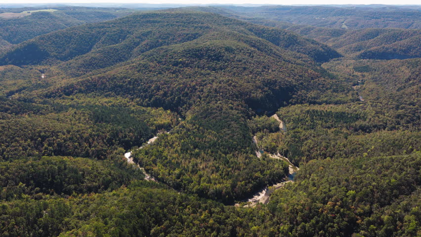 Elevated aerial establishing across winding river in forested valleys and layered hills stretching into distance, Ozark National Forest autumn glow