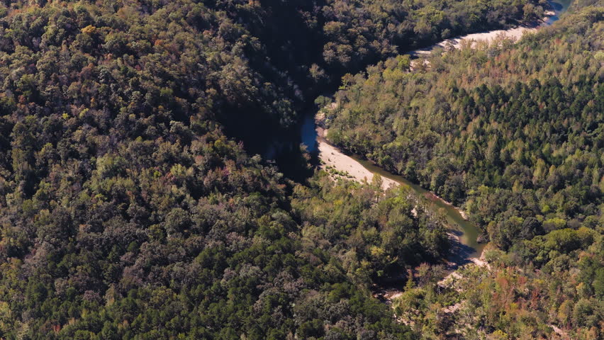 Aerial telephoto pan across pale sandy river curving along forest edge beside dense wooded terrain, Ozark National Forest