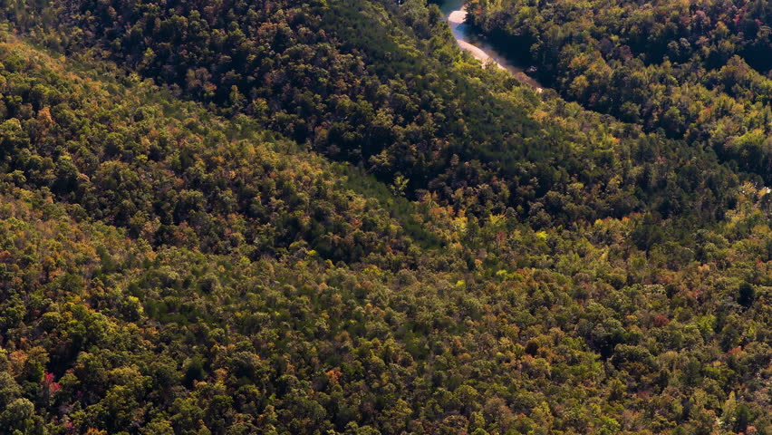 Oblique aerial of sunlit hills covered in forest with deep shadows shaping the terrain, winding river with sandy banks, Ozark National Forest