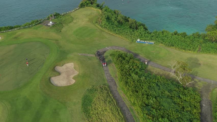 High aerial view of a stunning golf course on a cliff overlooking the ocean. Golfers are putting on the green next to sand traps