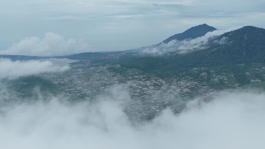 Stunning panoramic view from above the clouds of a balinese town and mountain landscape. The mist moves gracefully across the scenery
