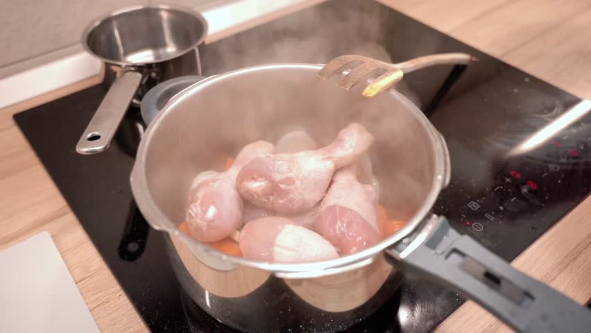 A pot of chicken is cooking on a stove. The steam from the pot is rising and the chicken is browning
