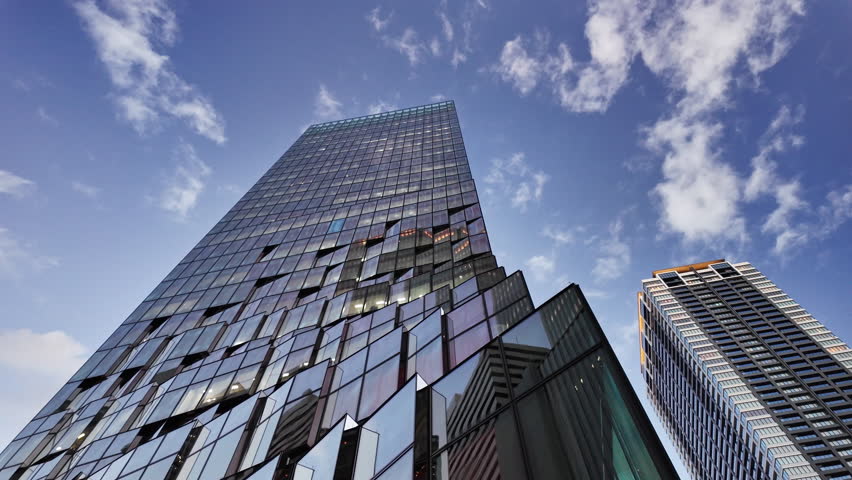 Modern skyscraper in Umeda, Osaka, Japan, shot from a low angle against a clear blue sky with white clouds. Professional business and architectural footage in 4K 60P ProRes.