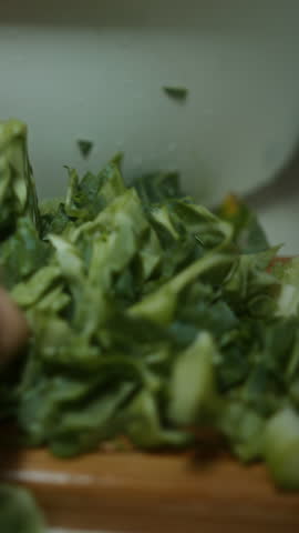 Close-up of hands finely chopping leafy green vegetables on a wooden cutting board, preparing healthy ingredients for cooking, vertical video