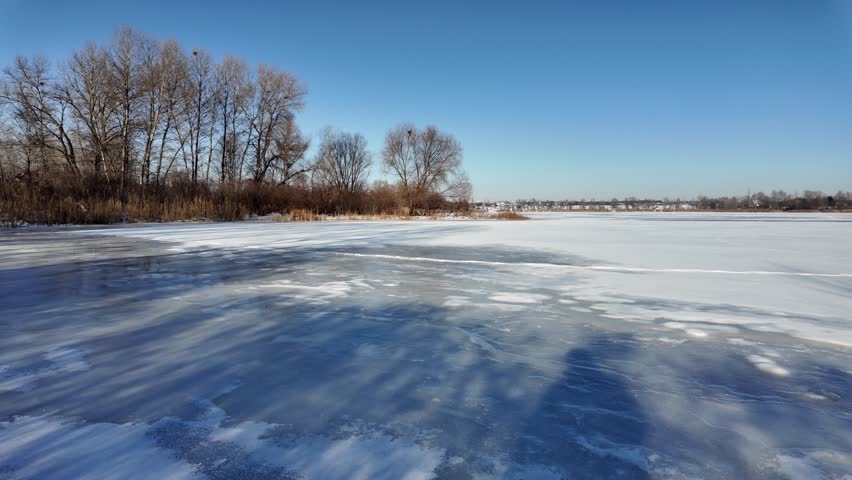 
In the heart of a tranquil winter wonderland, a frozen lake stretches out like a vast, shimmering mirror, cradled beneath an expansive bright blue sky that seems to pulse with clarity and infinite depth. The air is crisp and biting, carrying the faint whisper of distant winds through the barren landscape, where silence reigns supreme, broken only by the occasional creak of ice settling under its own weight or the soft crunch of snow beneath unseen wildlife.
The lake