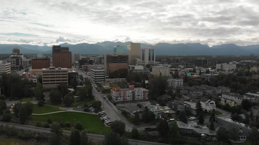 Alaska, Anchorage, Aerial view of the capital with houses and streets, mountains and clouds in the background
