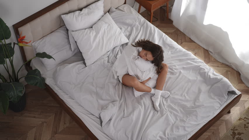 High angle view of a beautiful young woman enjoying a lazy morning, rolling and relaxing in a cozy bed with soft white linens