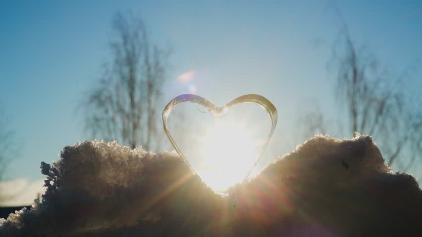 Heart-shaped frozen soap structure on snow, glowing in sunlight and symbolizing winter cold, love, and abstract beauty.